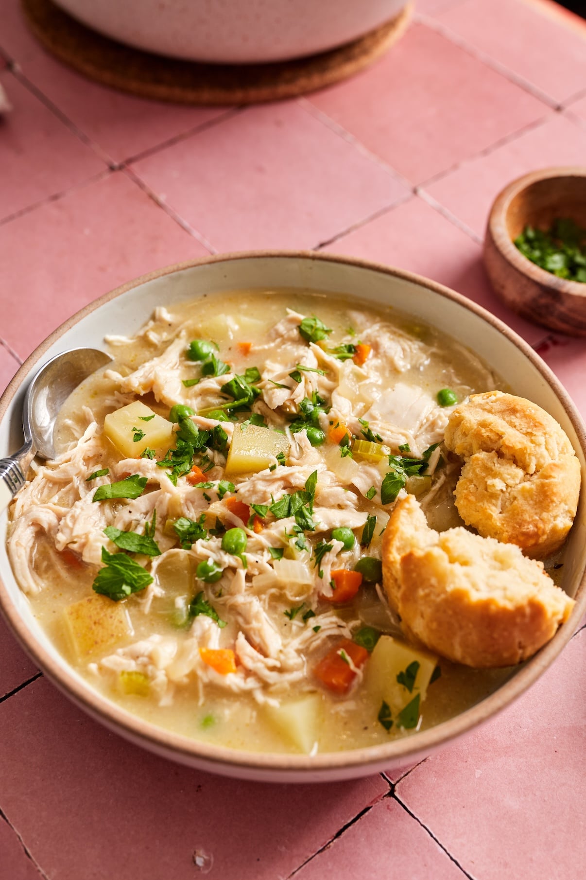A close up of a bowl filled with creamy chicken pot pie soup with a fluffy biscuit on top. 