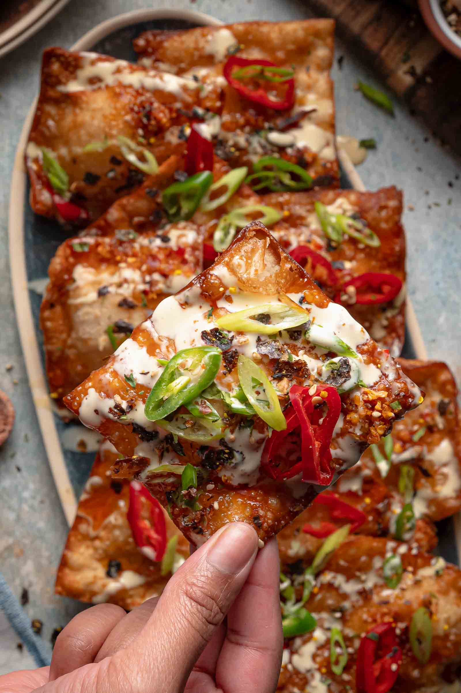 A hand lifting one loaded crab rangoon crisp off the platter, toppings piled on top.