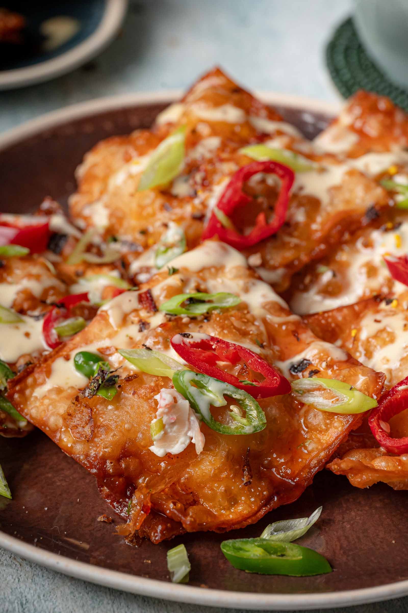 Close-up of crab rangoon nachos on a brown plate, the crab filling visible at a broken edge under the drizzle.