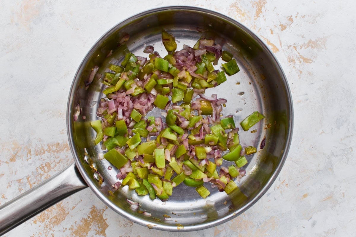 Diced red onion and green bell pepper cooking in a skillet.