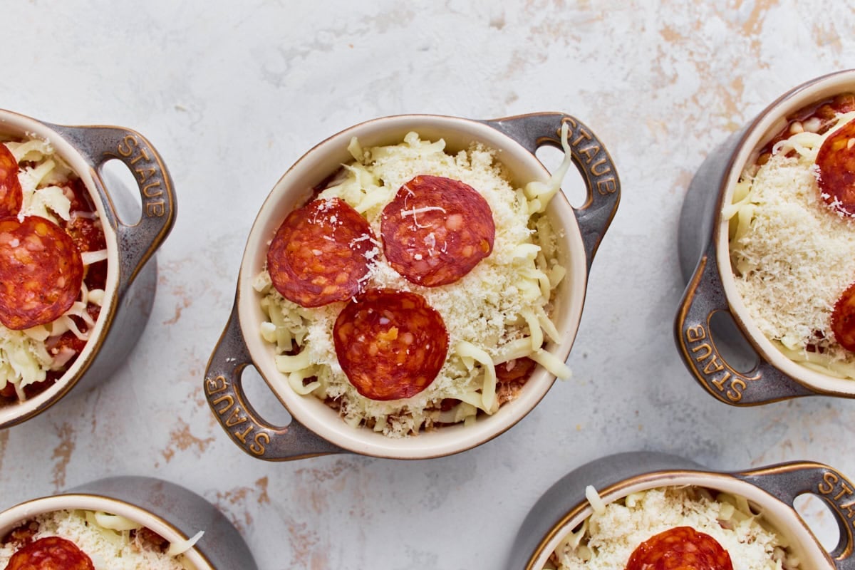 Mini ramekins topped with shredded mozzarella, Parmesan, and pepperoni before baking.