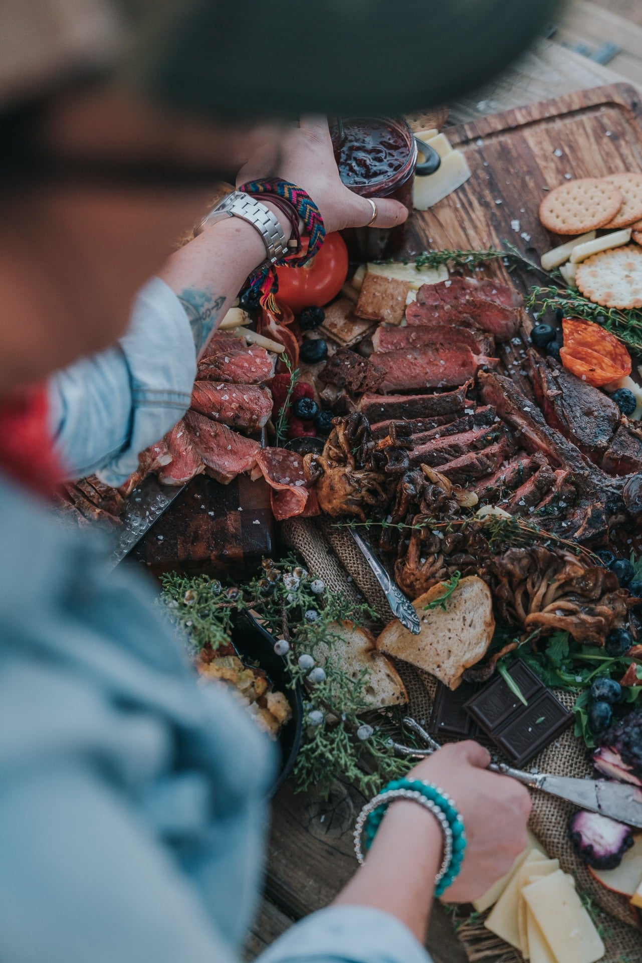 Reaching over an abundant table of grilled steaks.
