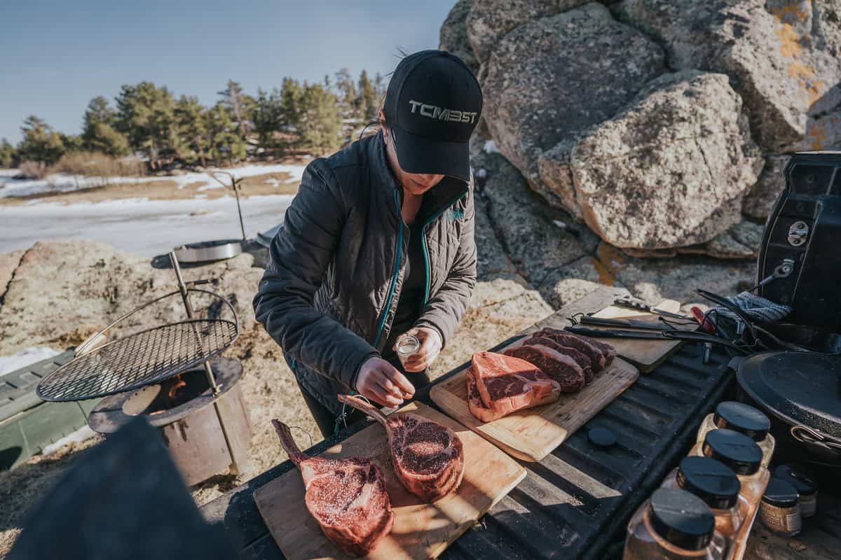 GirlCarnivore seasoning steaks on a truck bed.