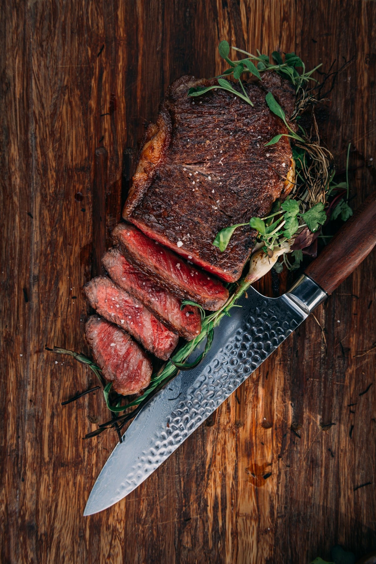 Sliced steak to show a red medium rare edge to edge center on wooden cutting board.