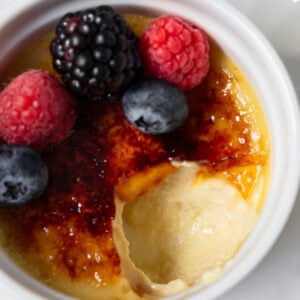 Dairy-free crème brûlée with a crackly caramelized sugar top, garnished with fresh berries in a white ramekin.