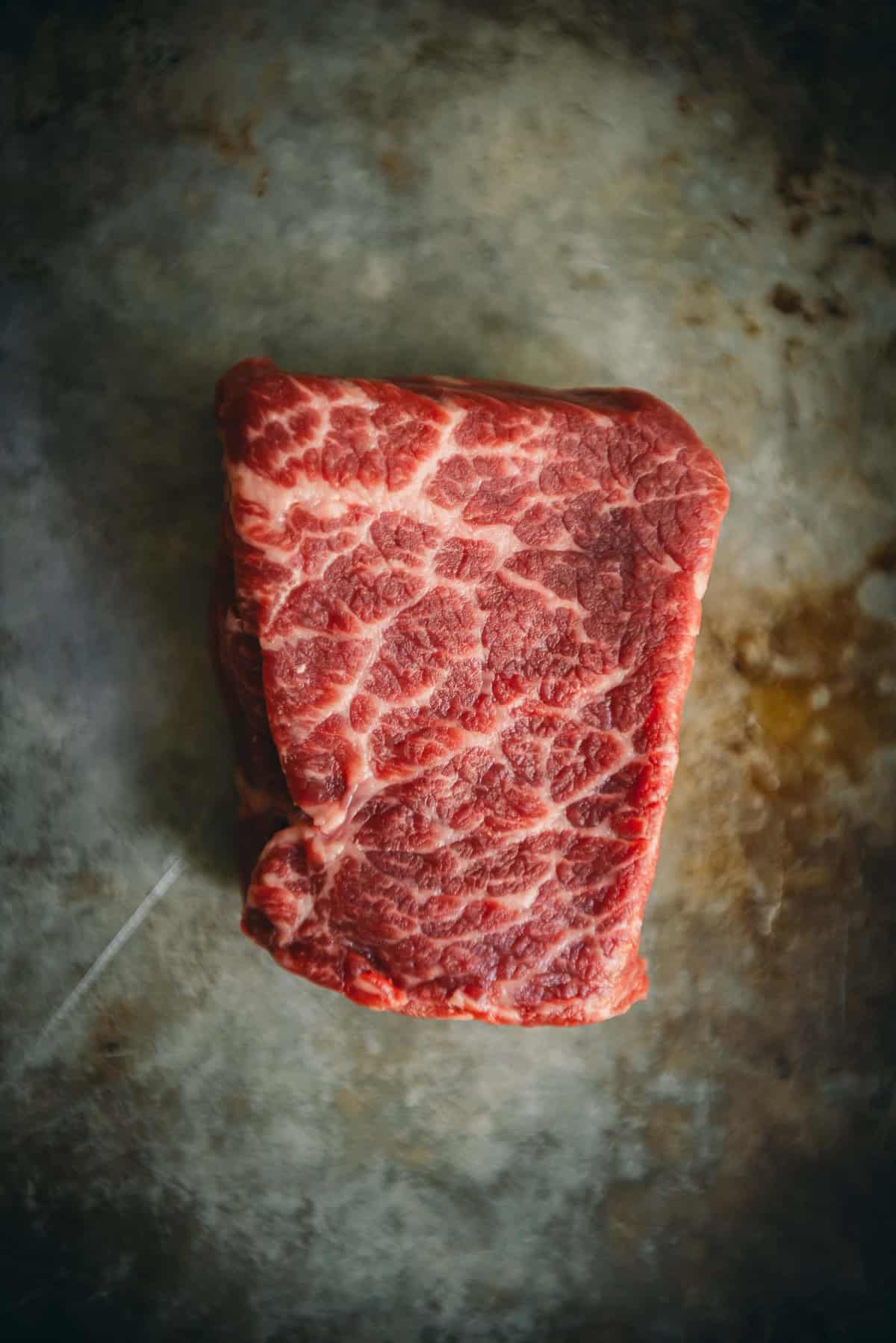 Petit Denver steak on a black serving tray to show marbling and grain. 
