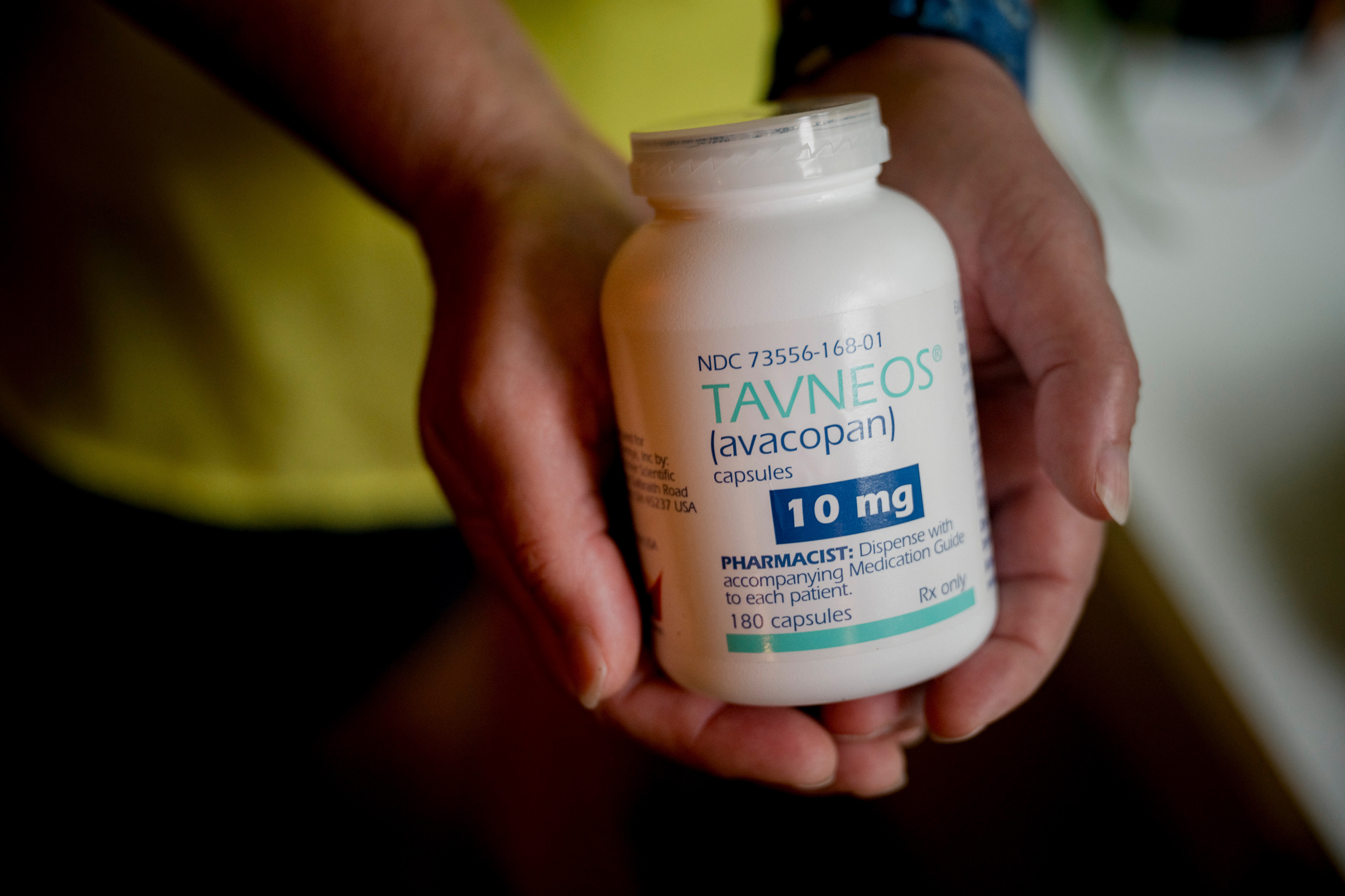 A pair of hands holds a bottle of Amgen's drug Tavneos.