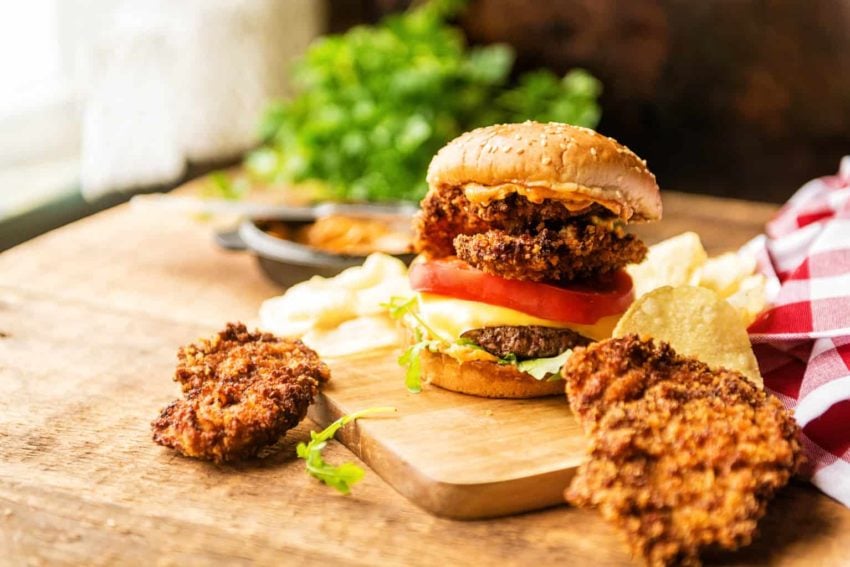 A surf and turf burger on a wooden cutting board.
