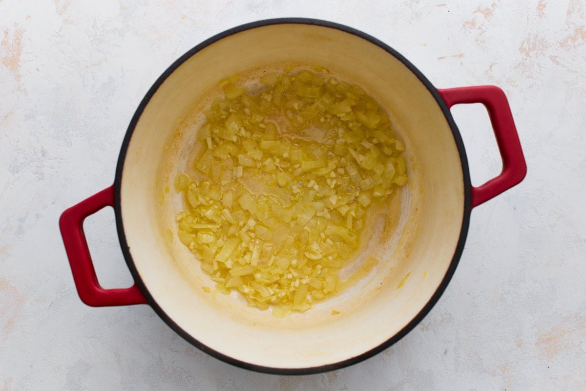 Softened, translucent onions and garlic cooking in butter in a red Dutch oven, the first step of gluten-free broccoli cheddar soup.