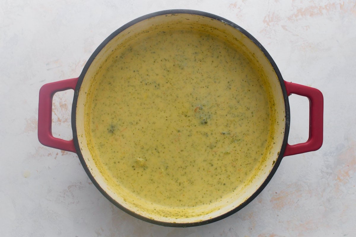 Thick, smooth, glossy gluten-free broccoli cheddar soup in a red Dutch oven after the cheddar cheese has fully melted in.