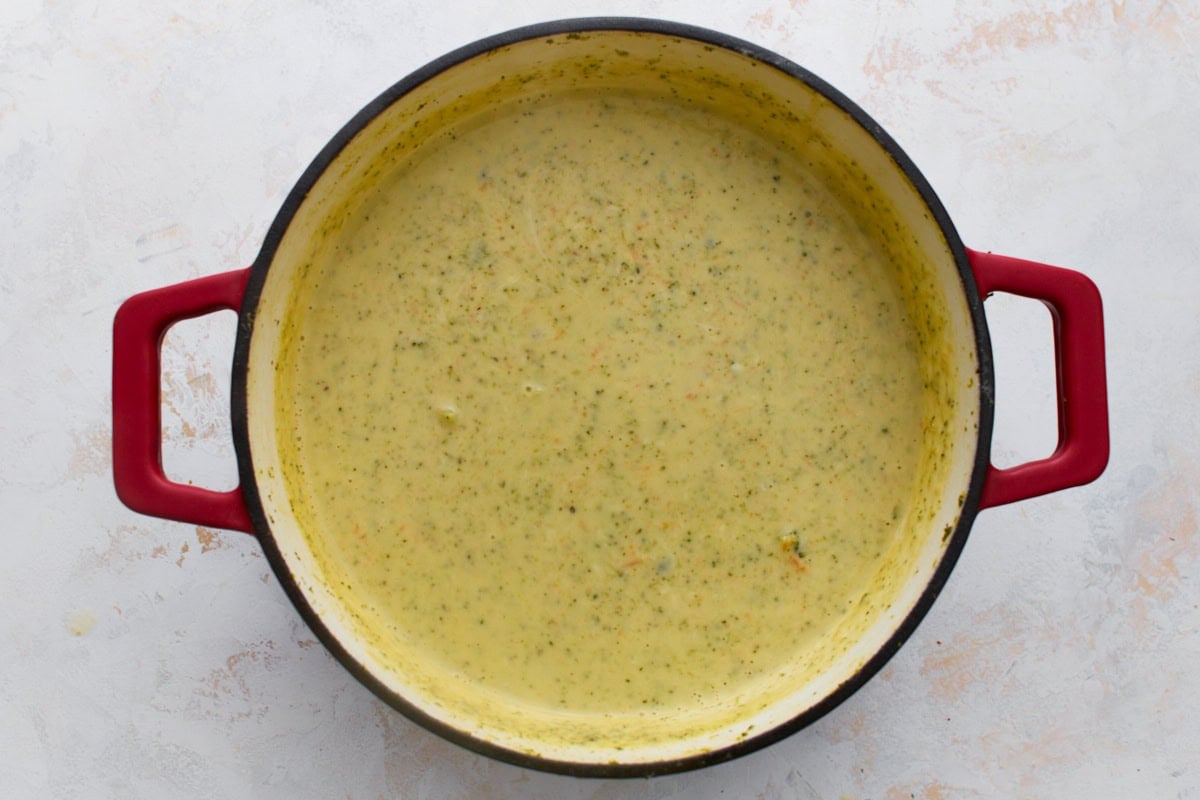 Thick, smooth, glossy gluten-free broccoli cheddar soup in a red Dutch oven after the cheddar cheese has fully melted in.