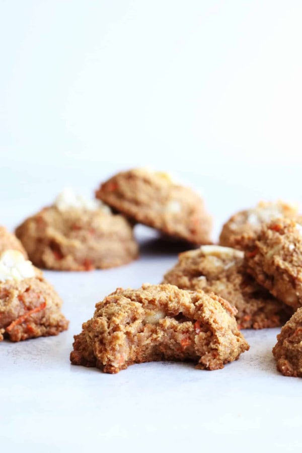 Gluten-Free Carrot Cake Macadamia Cookies from The Toasted Pine Nut on a pale blue surface. One has a bite taken out of it.