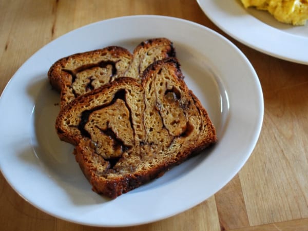 Two Slices of Gluten-Free Cinnamon Swirl Bread on white plate beside another plate with scrambled eggs.