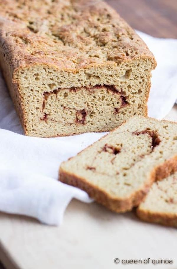 Loaf of gluten-free Cinnamon Swirl Bread with two slices laying down on white napkin and white counter.