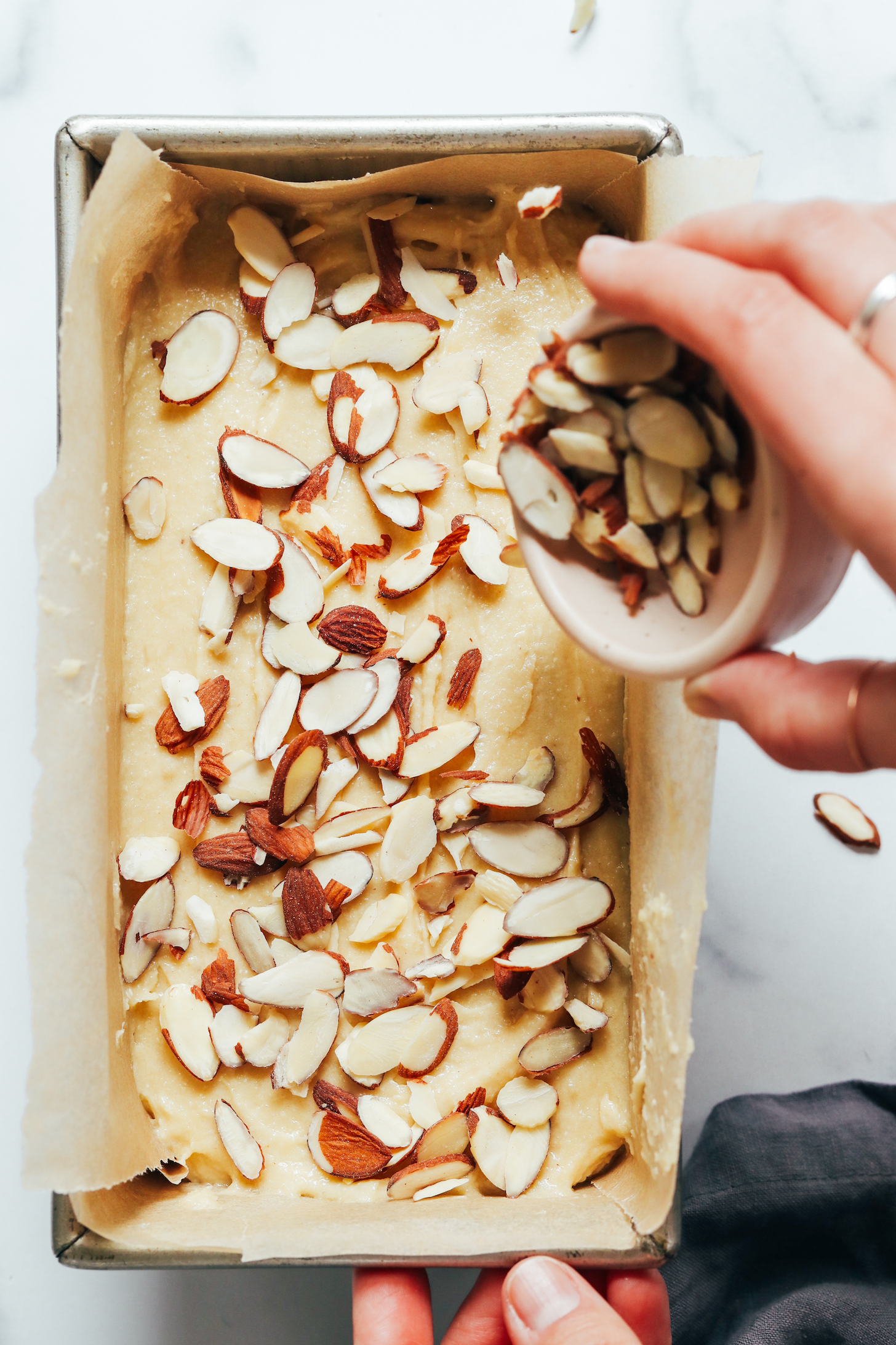 Sprinkling sliced almonds on top of cake batter in a loaf pan