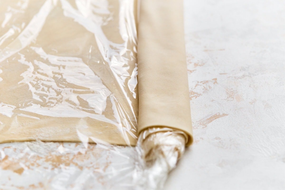 Gluten-free phyllo dough rolled up and wrapped tightly in plastic wrap for storing in the refrigerator.