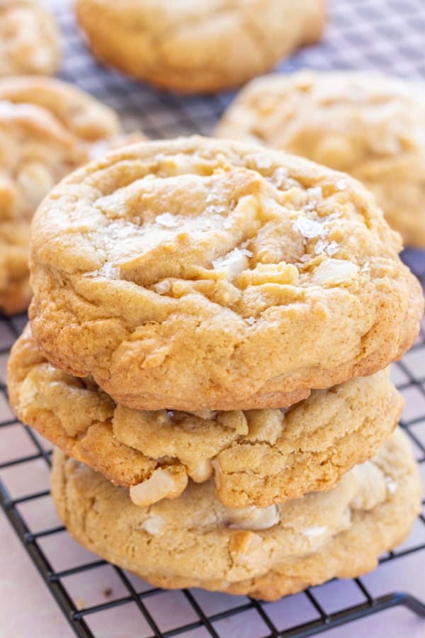 Gluten-Free White Chocolate Macadamia Nut Cookies from Life After Wheat on a black rectangular metal cooling rack above a pale pink surface. The three in front are stacked.