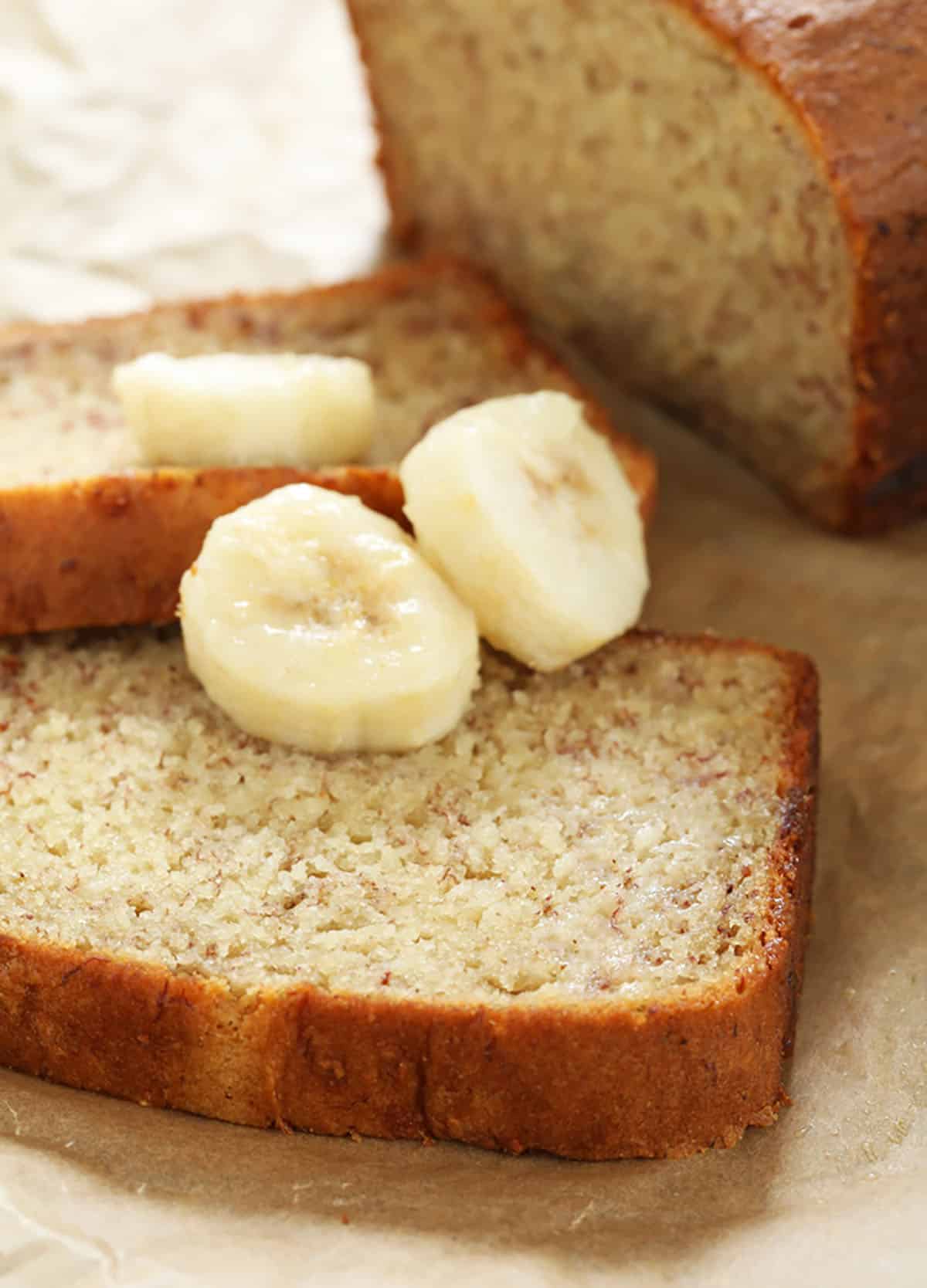 Closeup of a slice of the finished gluten free banana bread recipe with 3 slices of fresh bananas on brown paper.