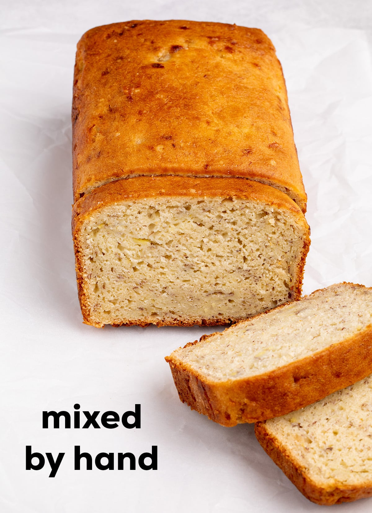 A fluffy loaf of banana bread with two slices cut from the front is shown with the text “mixed by hand.”