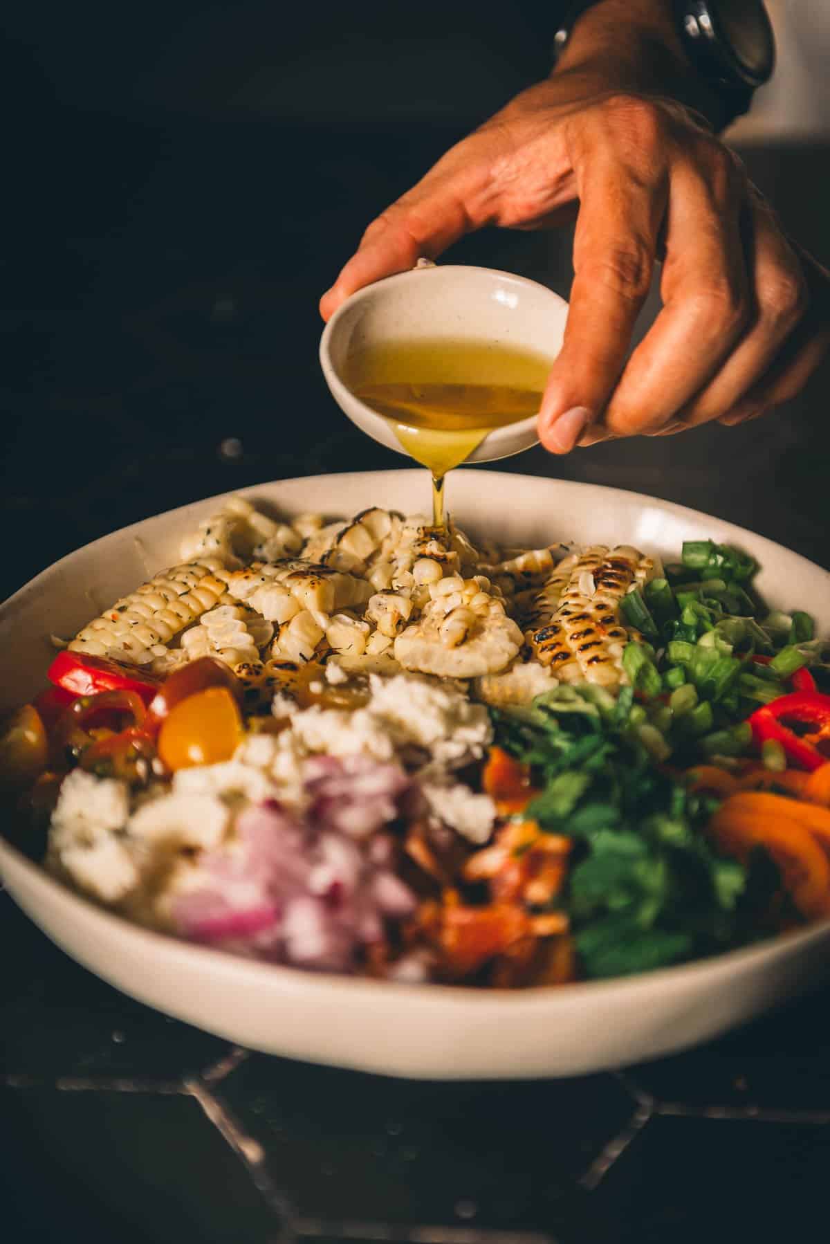Hand pouring oil into bowl with ingredients. 
