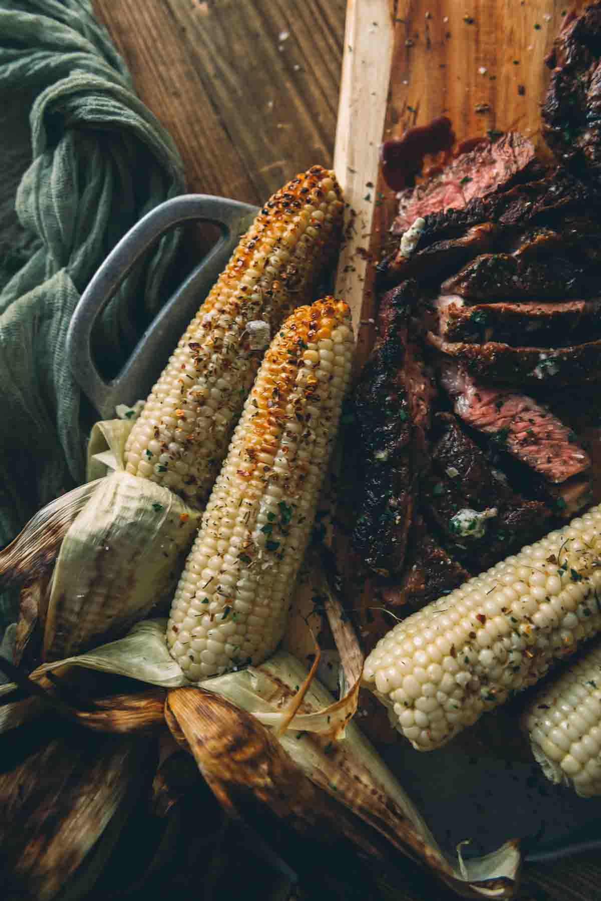 Overhead shot of grilled corn with husks peeled back on a platter garnished with seasonings for serving.