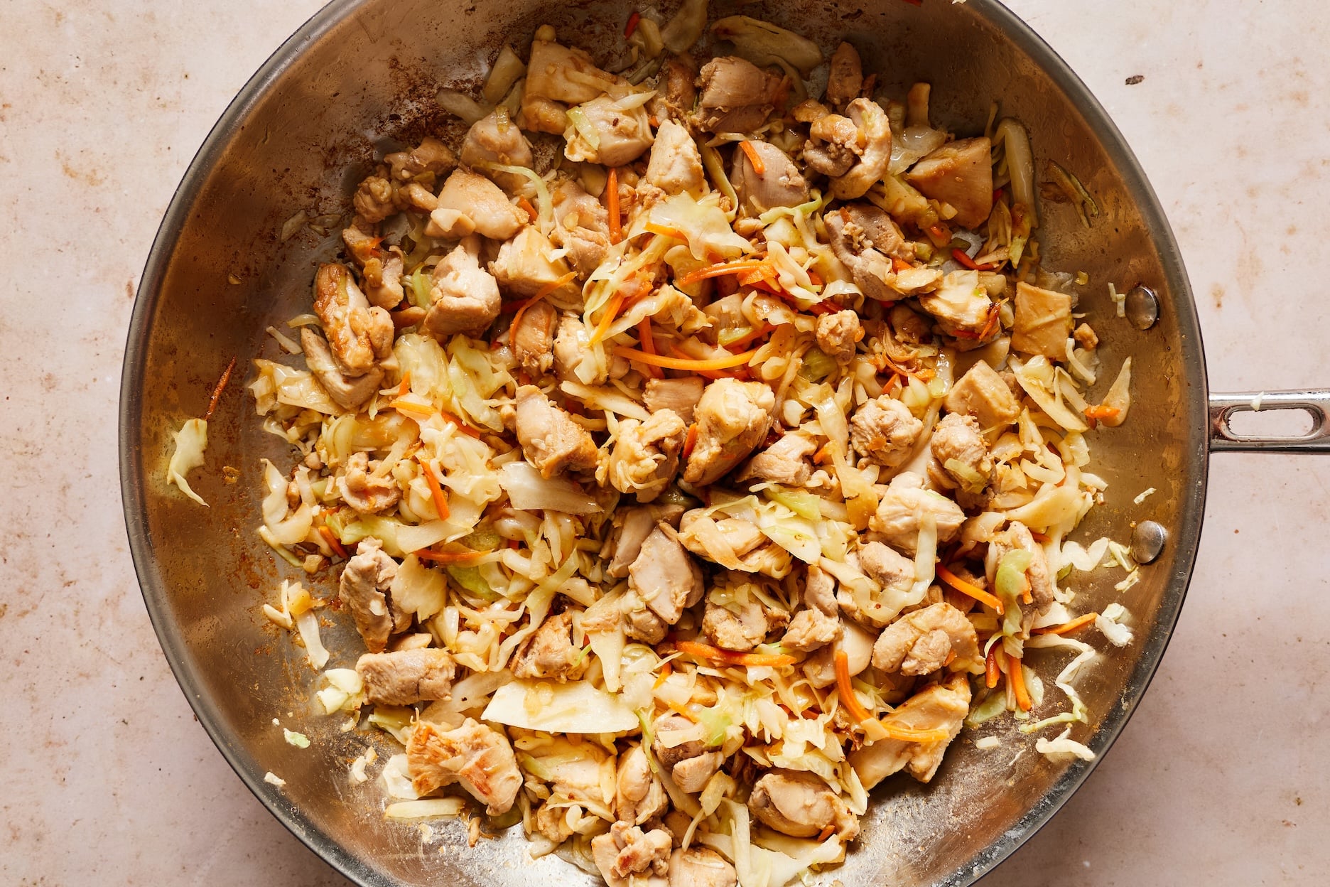 Chicken and coleslaw mix cooking in sesame oil in a large skillet with fresh garlic added.