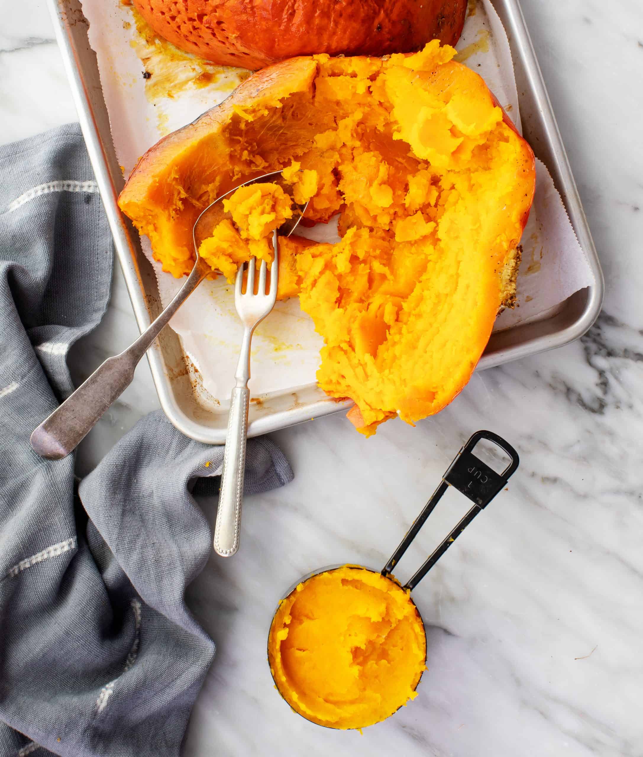 Roasted pumpkin on a baking sheet with measuring cup