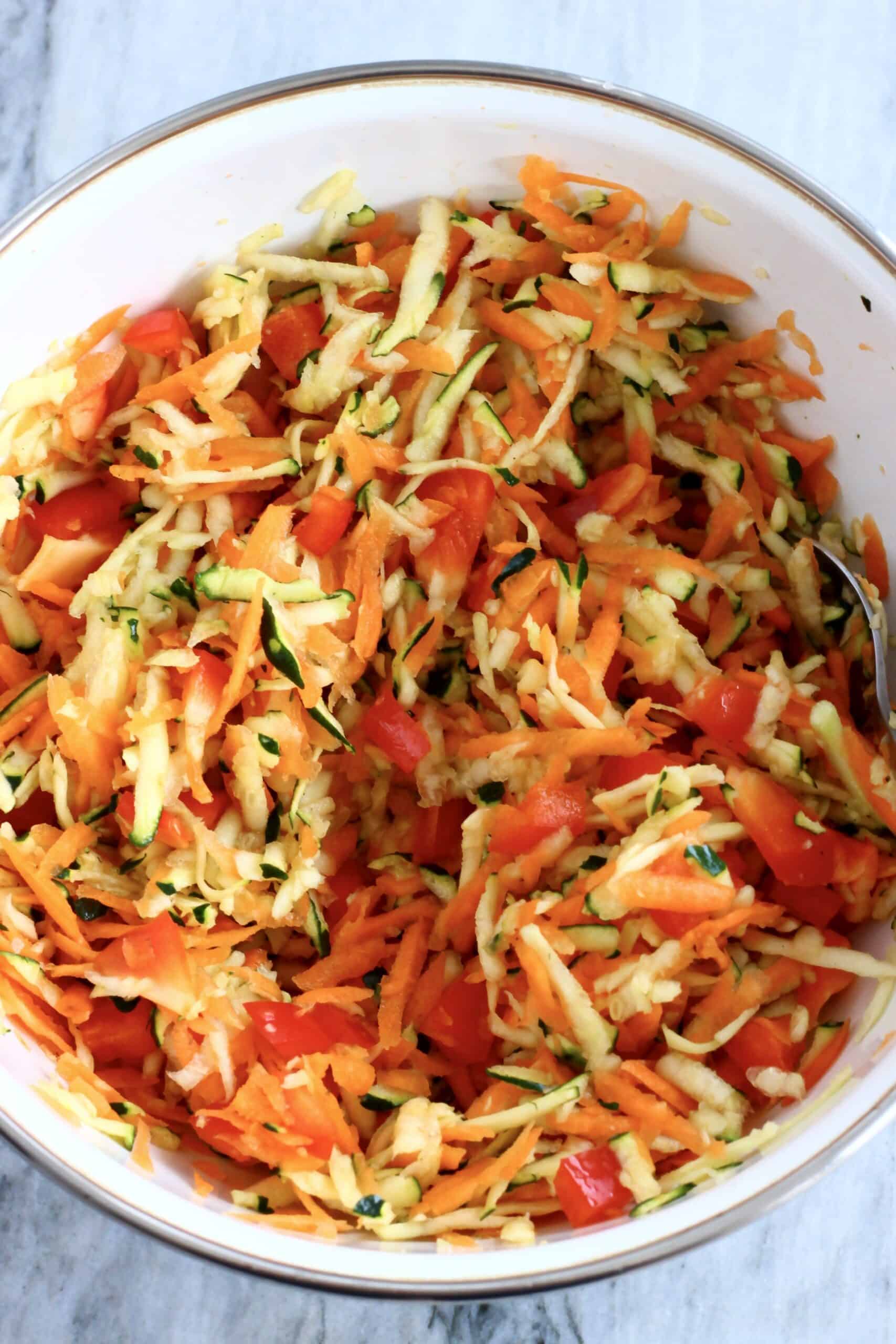 Grated carrot, zucchini and diced red bell pepper in a bowl