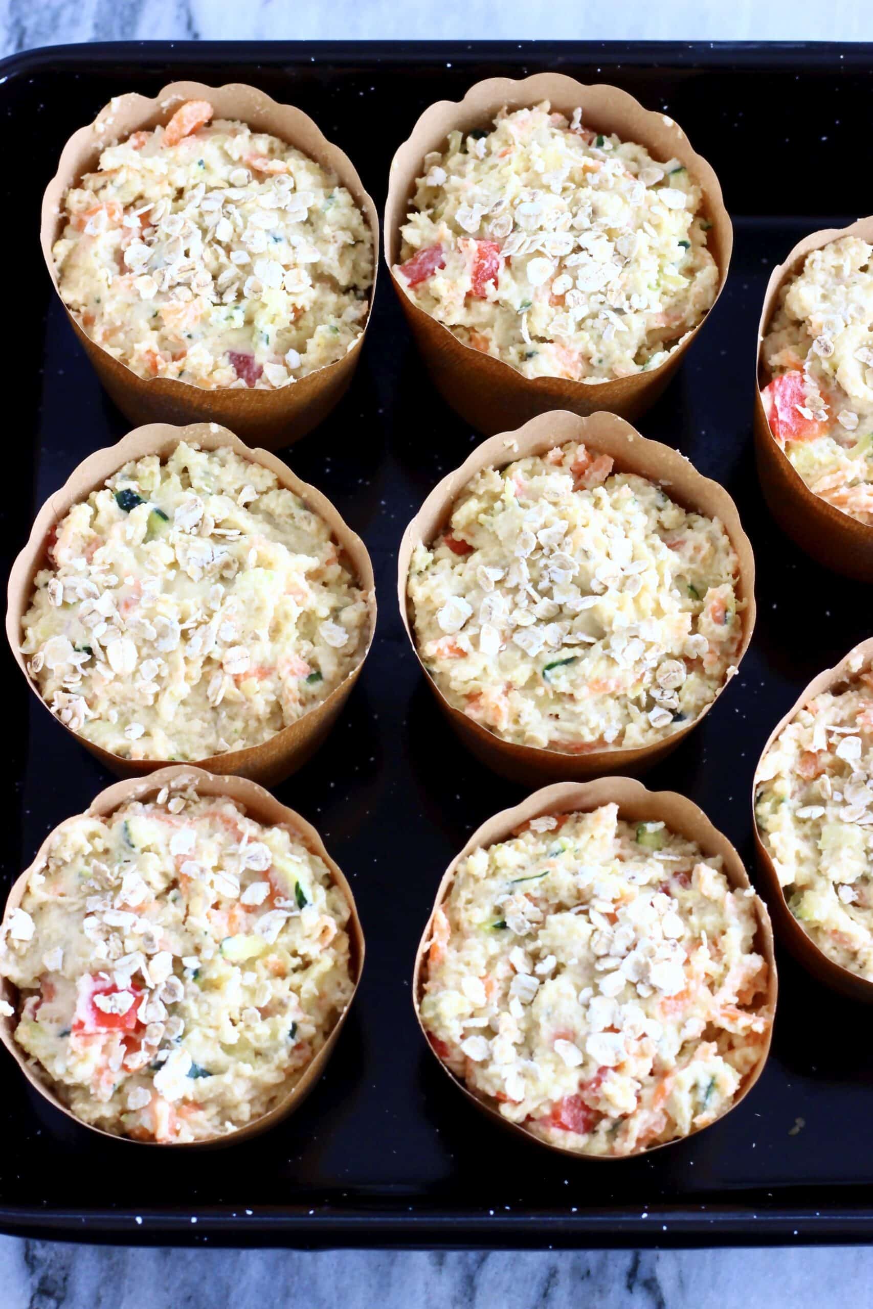Raw gluten-free vegan savoury vegetable muffins batter sprinkled with oats in muffin cases in a muffin tin