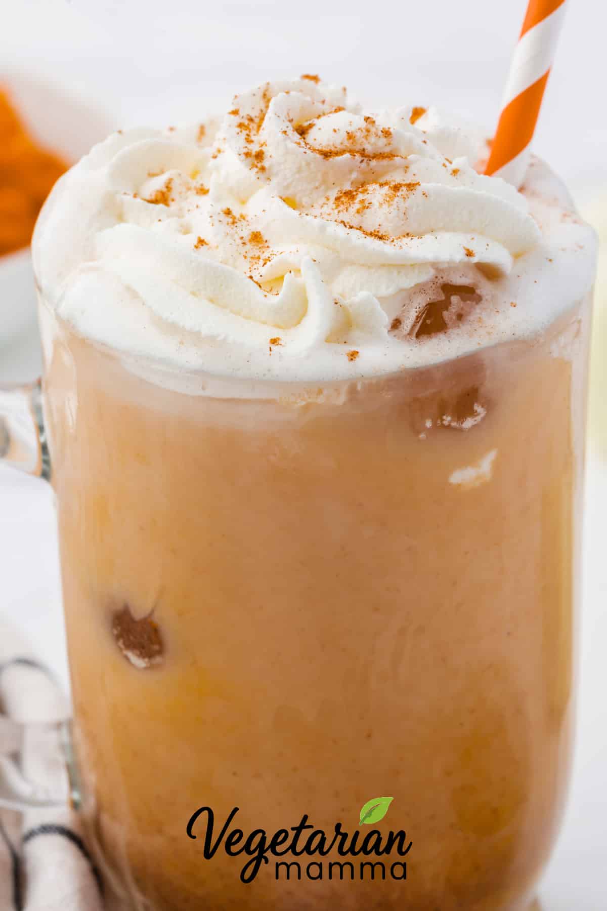 Closeup of a homemade iced pumpkin spice latte with an orange and white striped straw
