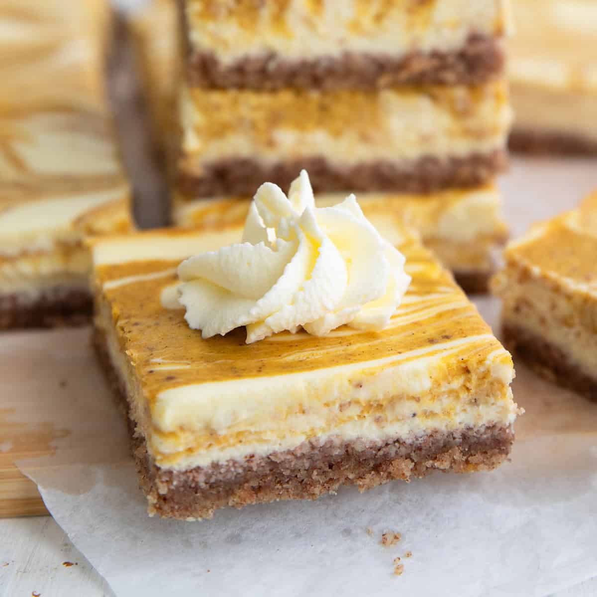 Close up shot of a keto pumpkin swirl cheesecake bar with a dollop of whipped cream on top.