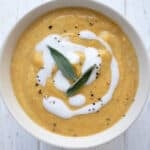 Top down image of a bowl of Keto Pumpkin Soup with a swirl of cream and two sage leaves on top.
