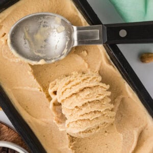 Overhead view of banana peanut butter nice cream being scooped from a black loaf pan with an ice cream scoop