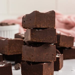 Stack of gluten-free dairy-free chocolate fudge squares topped with flaky sea salt, with chocolate chips scattered around and a pink cloth in the background