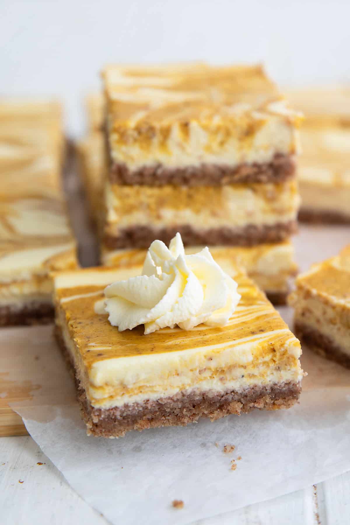 A keto pumpkin swirl cheesecake bar on a cutting board, with a stack of more cheesecake bars in the background.