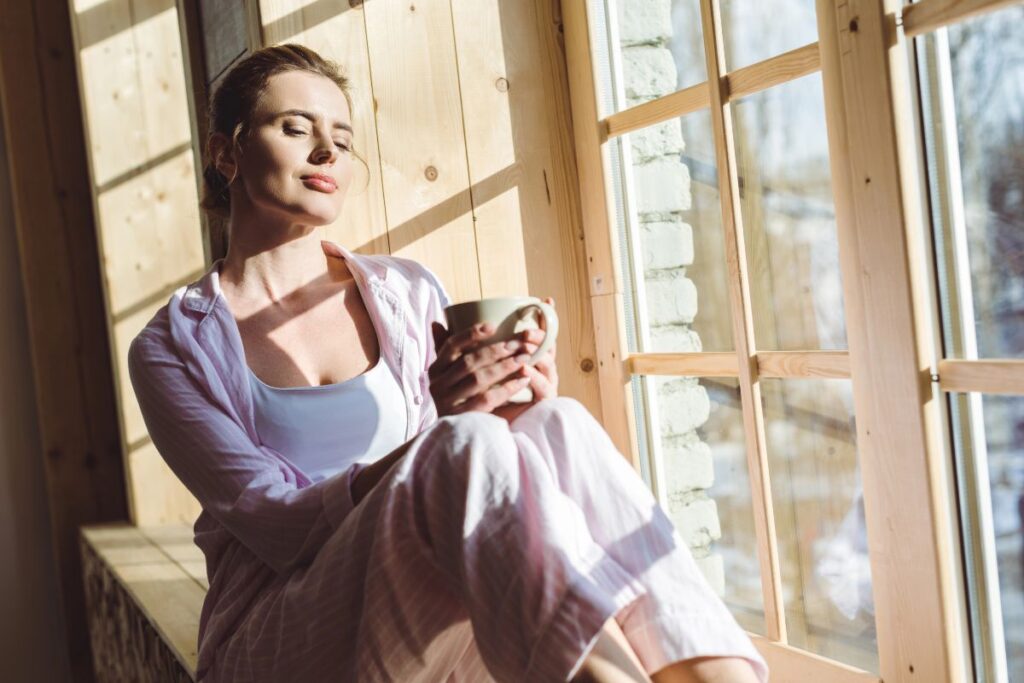 Woman relaxing by a sunny window with a warm drink.