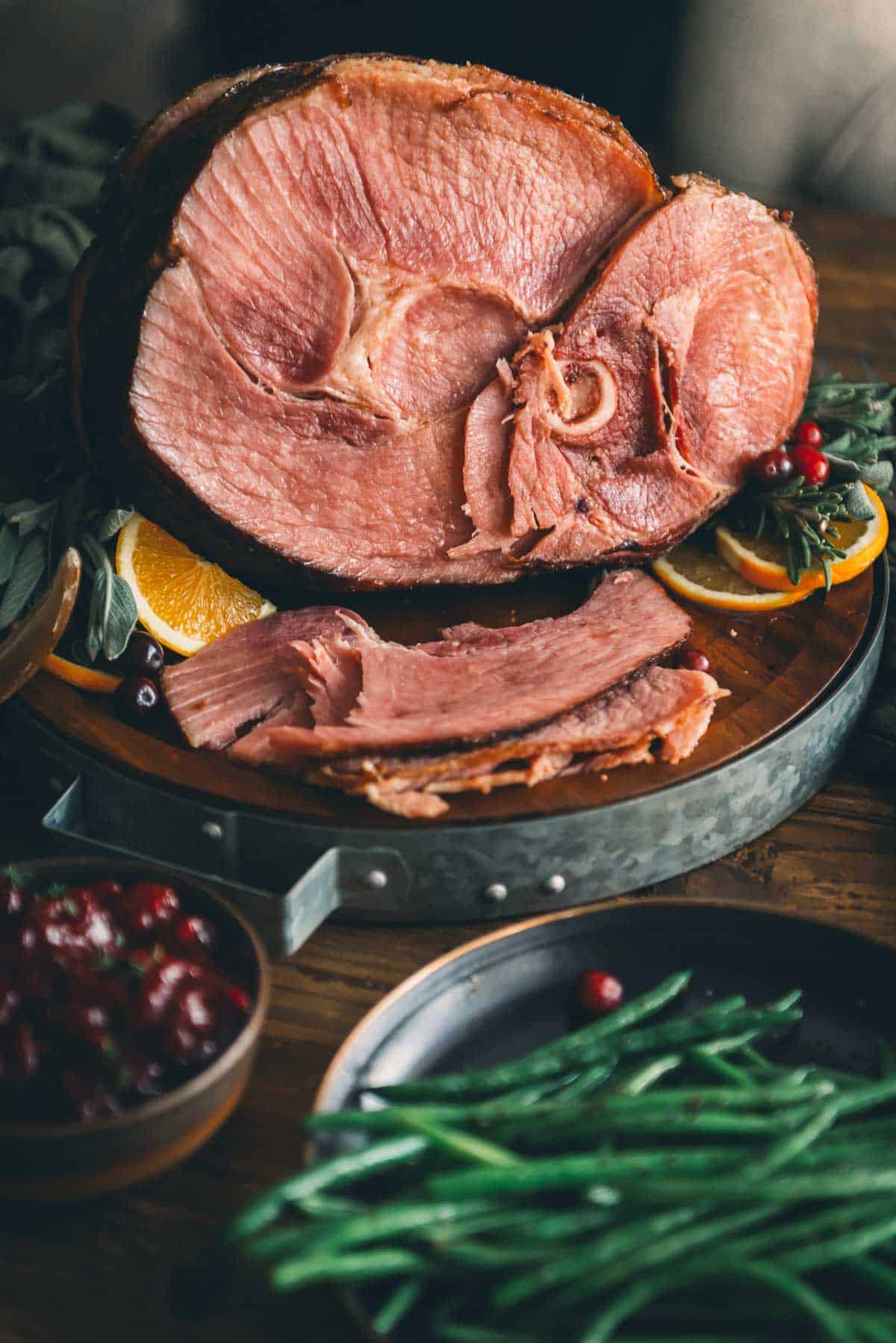 A spiral ham with green beans and oranges on a wooden board.