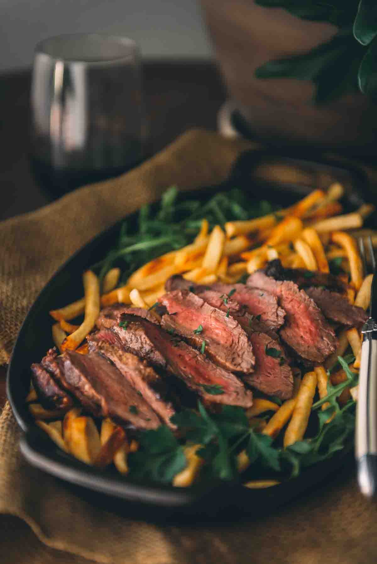 Plate filled with steak and a glass of wine in the background. 