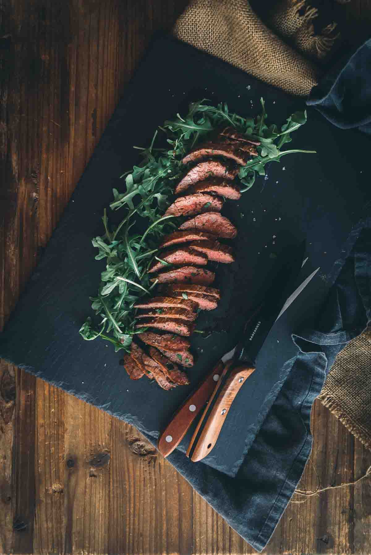 Overhead rustic wooden table with slate cutting board and a slices of cooked steak. 
