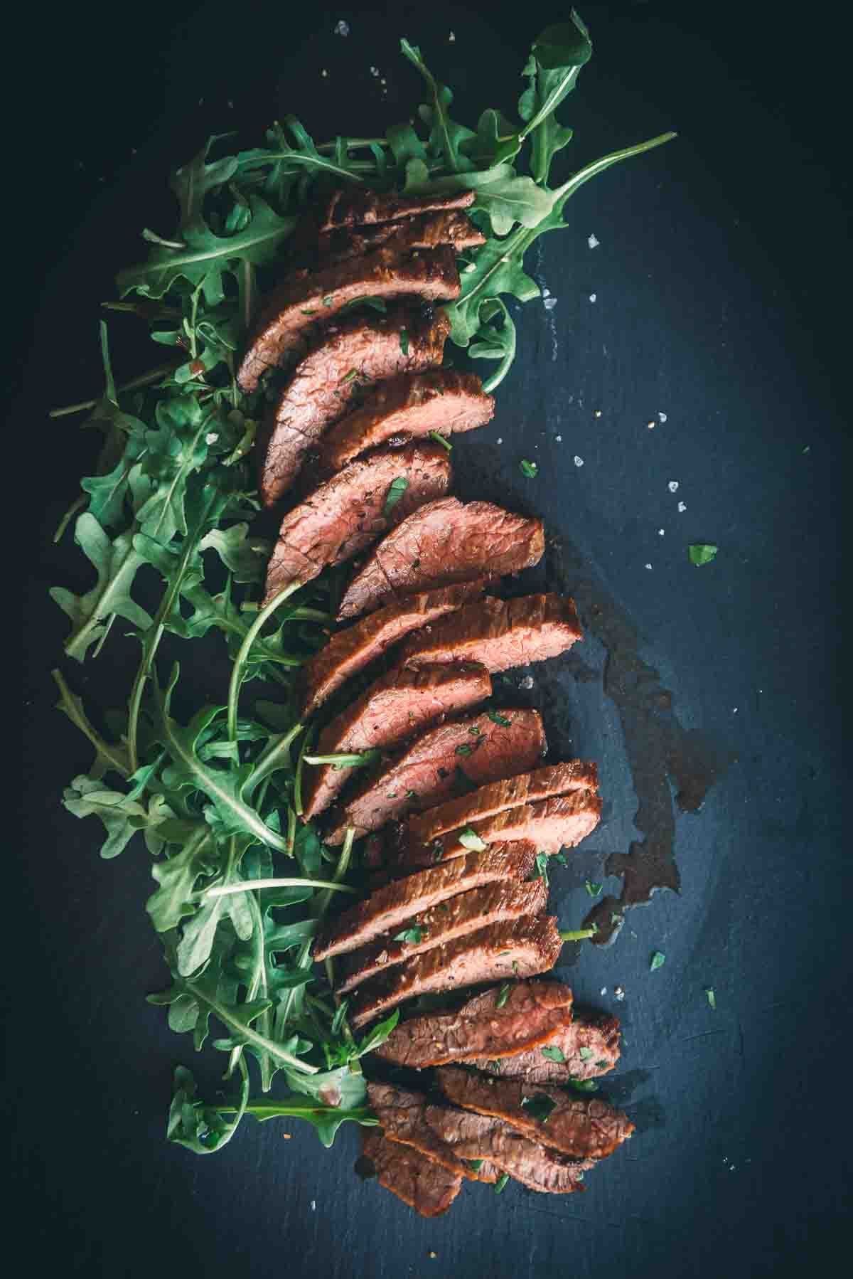 Steak on a black board sliced over arugula for serving. 