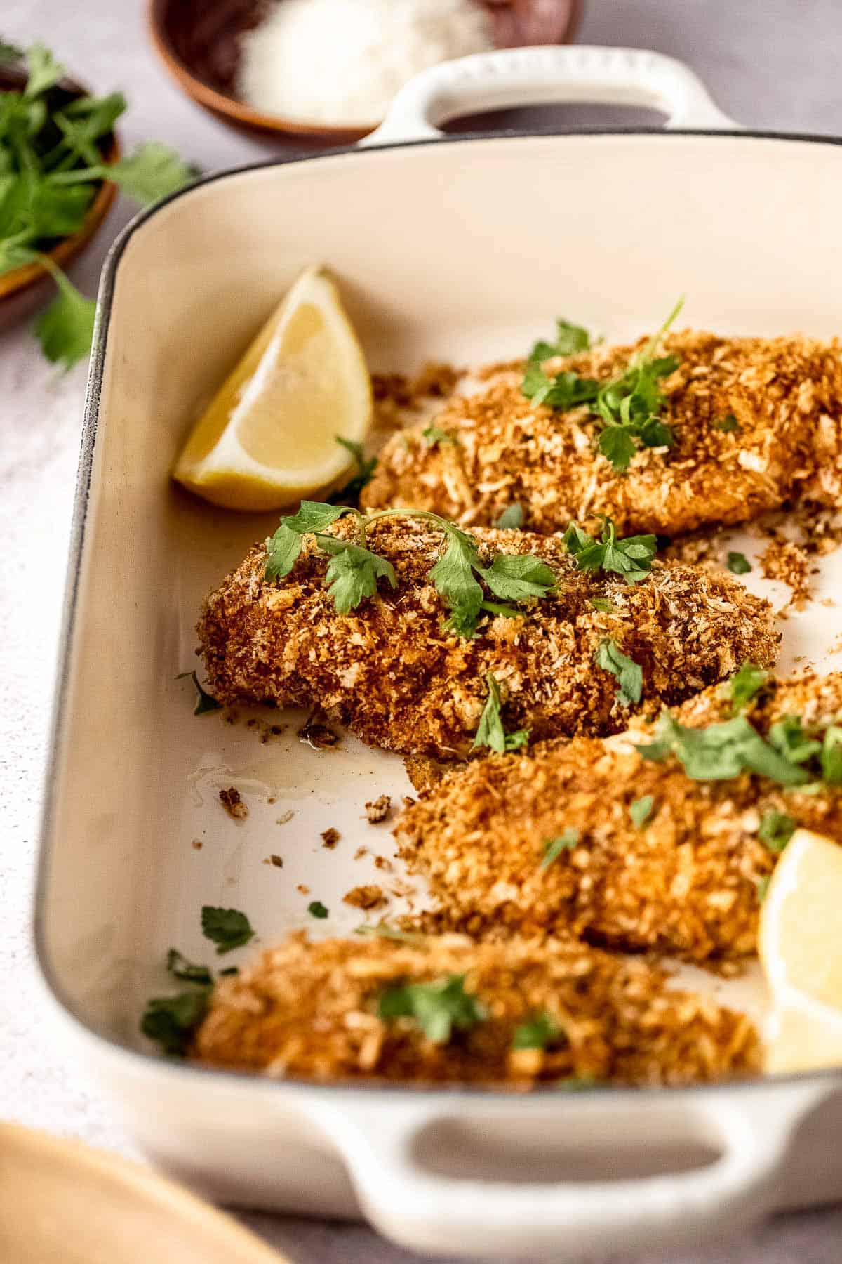 A baking dish with baked chicken and lemon wedges.