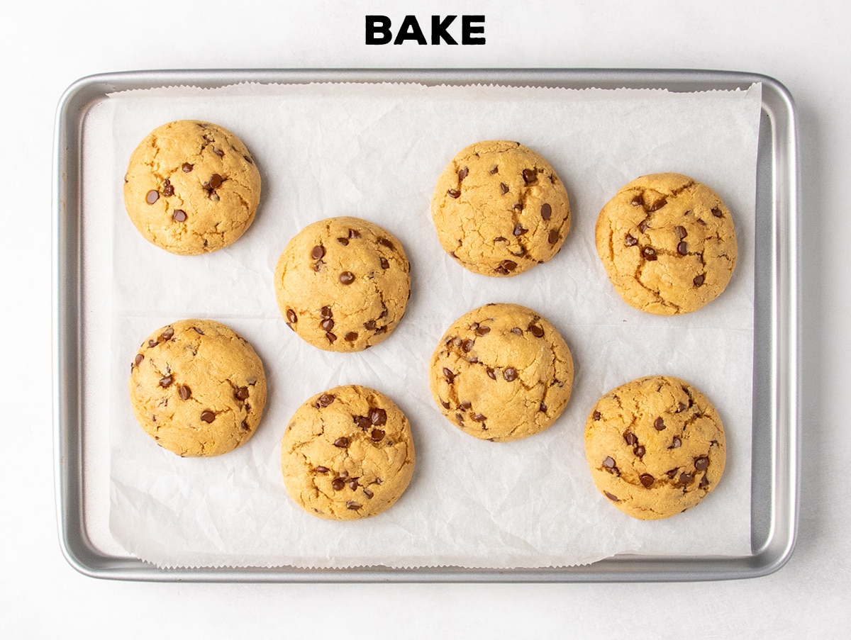 Eight baked light brown, round baked peanut butter chocolate chip cookies sit on a parchment-lined baking sheet; text reads “BAKE.”
