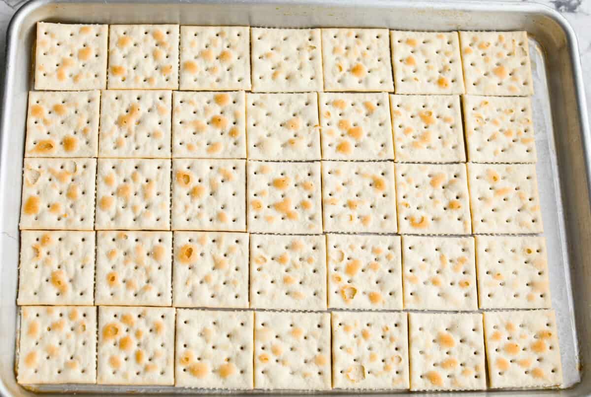 Pumpkin spice crack is Christmas crack with a fall twist! Buttery toffee, salty crackers, white chocolate, pumpkin pie spice, and crunchy praline pecans make this an easy treat you won’t be able to stop snacking on. Saltine crackers spread evenly on the baking sheet.