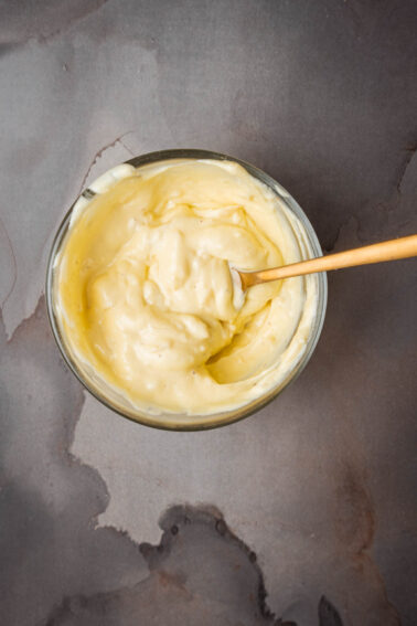 A bowl of roasted garlic aioli with a wooden spoon.