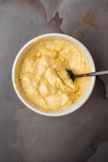 A bowl of yellow roasted squash aioli with a spoon in it.