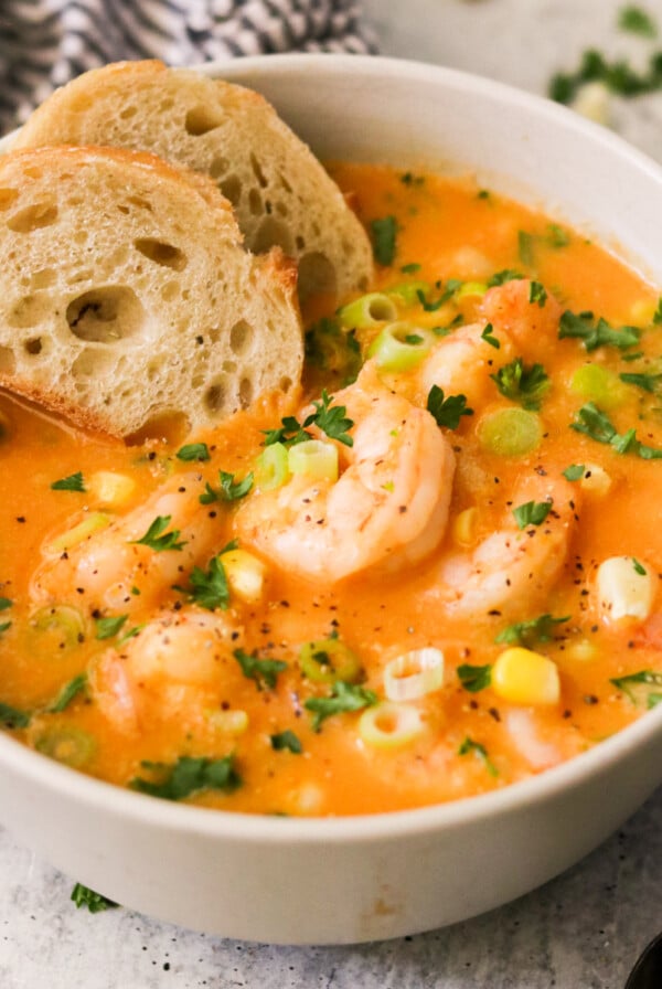 side view of a bowl of soup topped with garnishes and shrimp and two slices of bread.