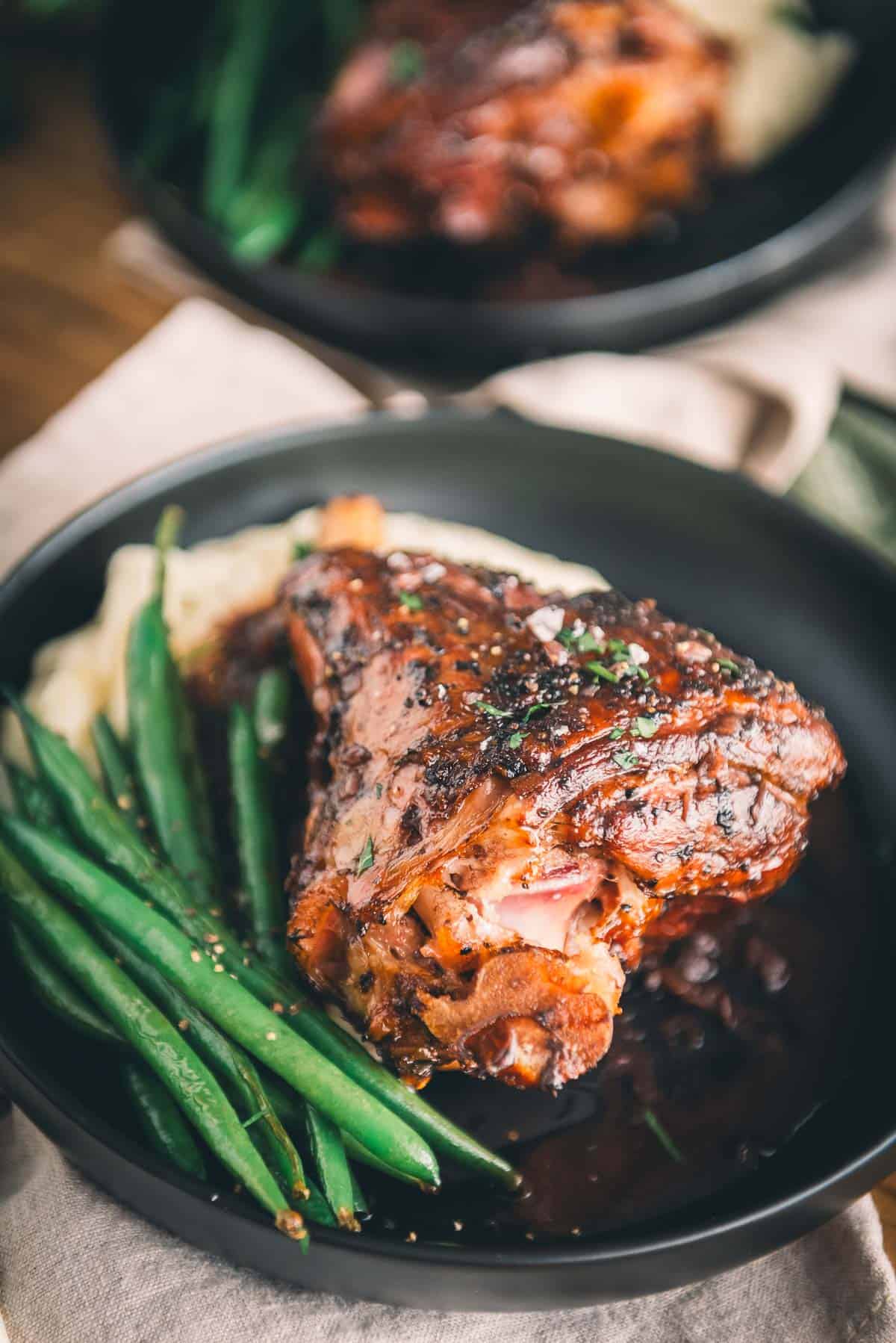 Lamb shank on a plate with green beans and mashed potatoes.