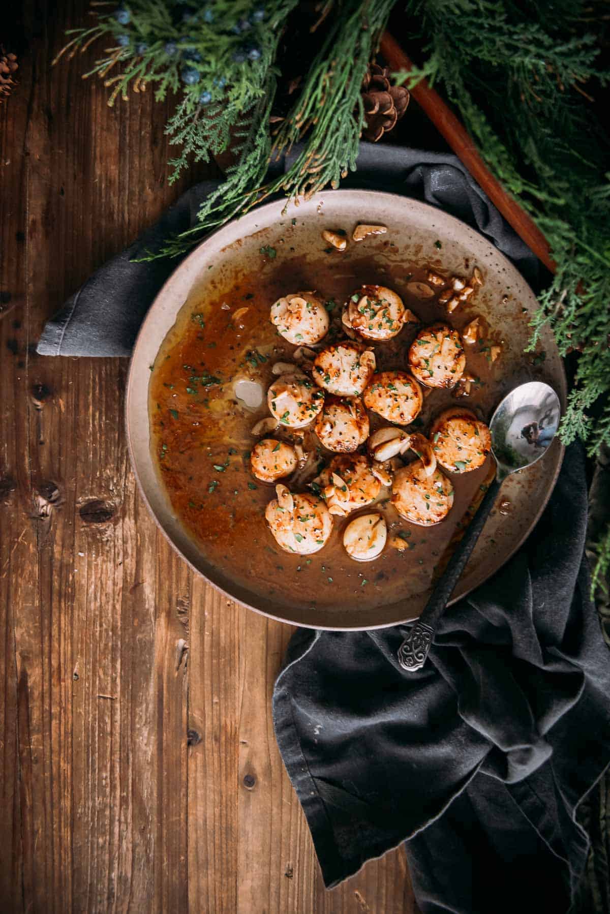 A bowl of scallops in a brown butter sauce on a wooden table.