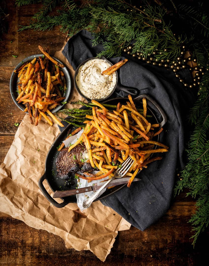 Dark and moody shot of steak frites with a pile of fries on the side.