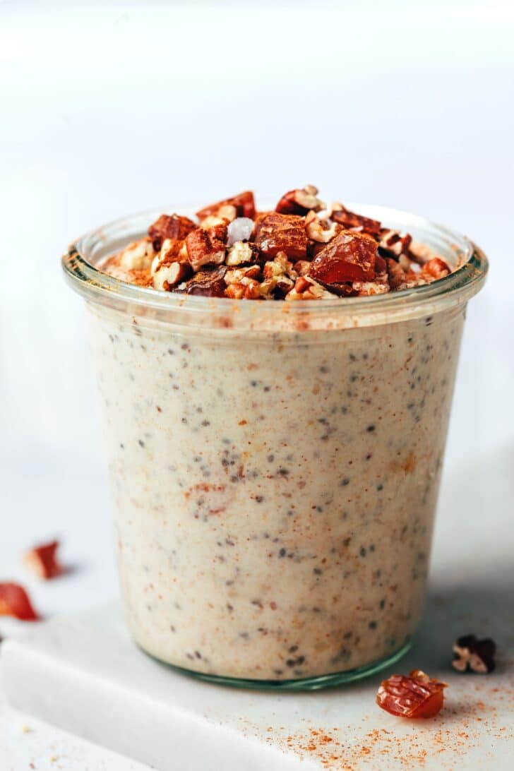 Sticky date overnight oats in a glass jar topped with chopped dates and pecans.